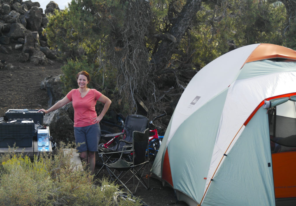 Woman standing by tent in a campground at Craters of the Moon National Monument while on a road trip.